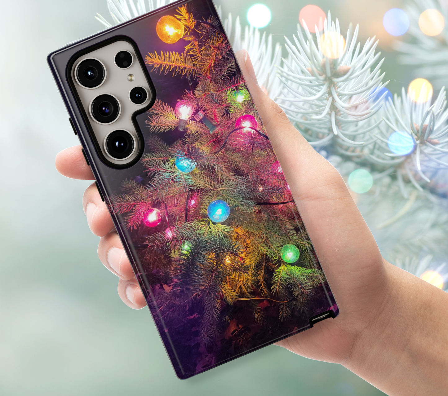 Phone case with Christmas tree design held by a hand, blurred Christmas lights in the background